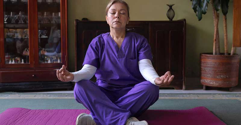 Nurse wearing purple scrubs in a meditation pose