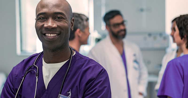 Nurse wearing purple scrubs smiling in hospital