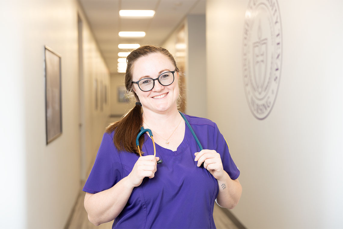 Smiling CTX nursing student in purple scrubs stands in a hallway